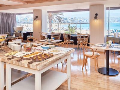 Sala colazione luminosa con vista sul mare, tavoli con dolci e sedie