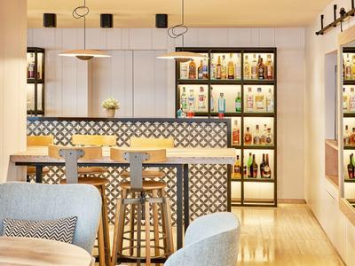 Area bar dell'hotel moderna con sgabelli, scaffali illuminati e posti a sedere accoglienti.