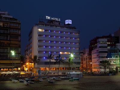 Illuminated hotel building at night with boats in the foreground by the water.