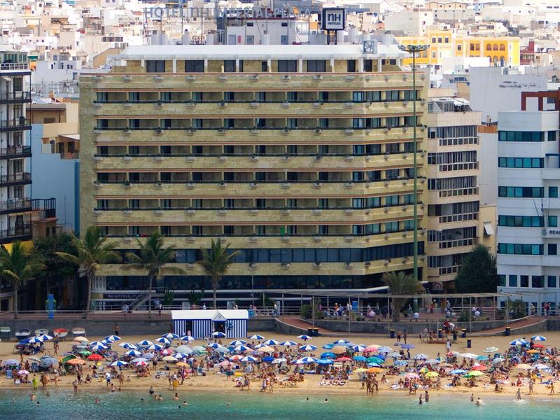 Edificio di hotel moderno vicino a una spiaggia affollata con ombrelloni e bagnanti