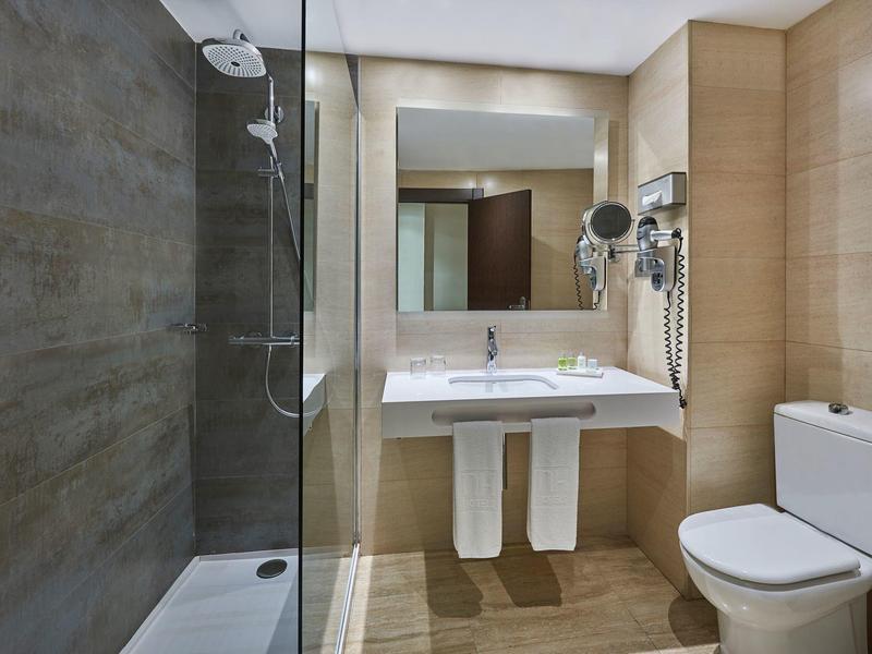 Bagno d'hotel moderno con doccia a filo pavimento, lavabo e WC in tonalità neutre.
