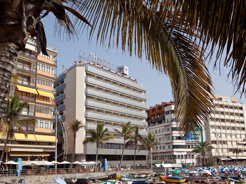 Diversi edifici di hotel con balconi, palme e una spiaggia affollata in primo piano.