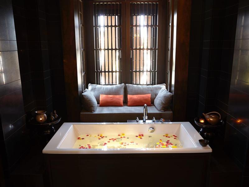 Vasca da bagno di lusso con petali di fiori, cuscini e finestra sullo sfondo.