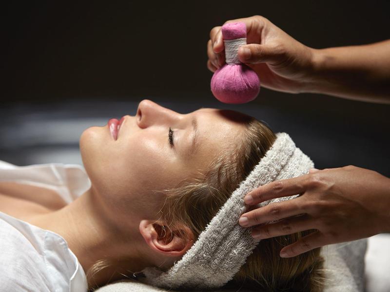 Donna rilassata durante trattamento viso con sacchetto di erbe alla spa.