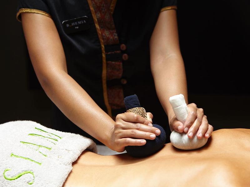 Una persona riceve un massaggio tradizionale con impacchi alle erbe sulla schiena.
