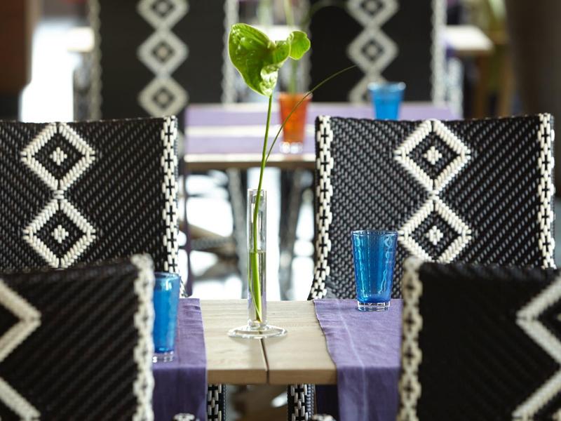 Primo piano di sedie nere con motivi bianchi e un bicchiere blu su un tavolo apparecchiato.
