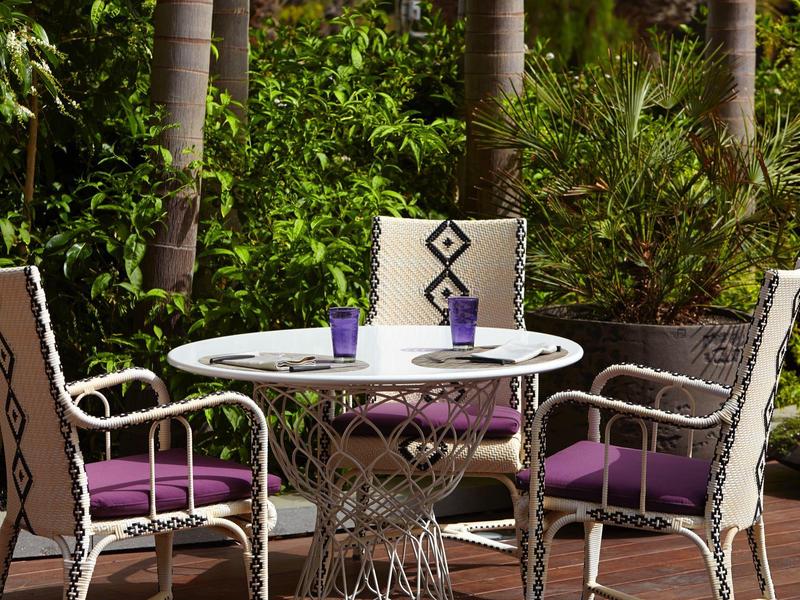 Tavolo da esterno con tre sedie e cuscini viola in un giardino verde