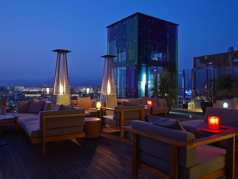 Accogliente terrazza sul tetto con aree salotto e illuminazione moderna al crepuscolo.