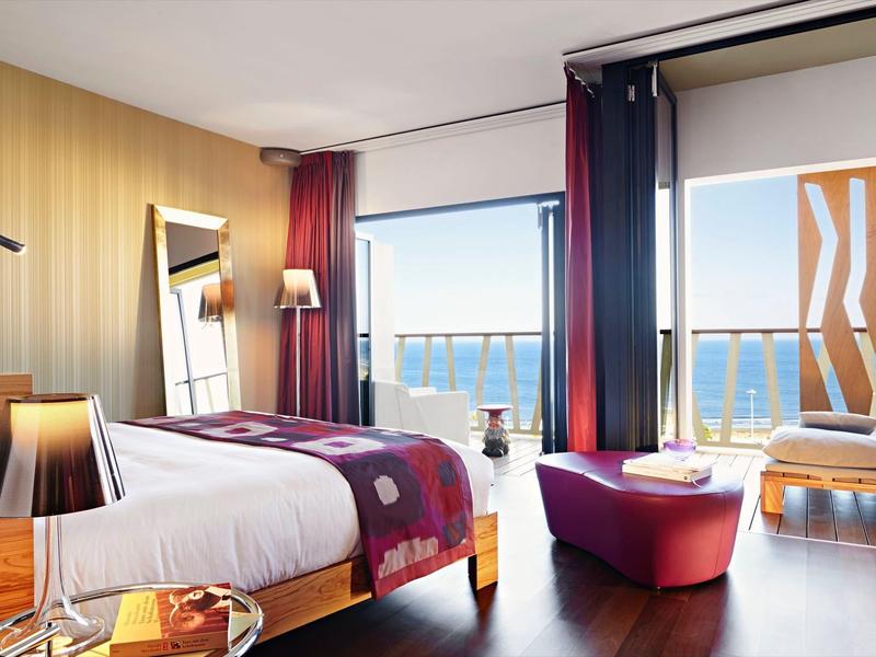 Camera d'albergo moderna con vista mare, letto matrimoniale e area salotto accogliente.