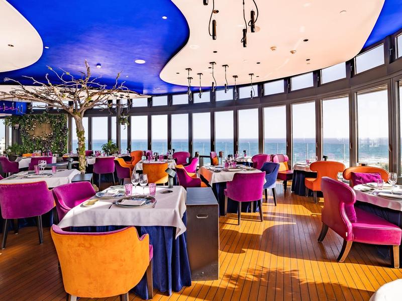 Ristorante moderno con sedie colorate e grandi finestre con vista sul mare.