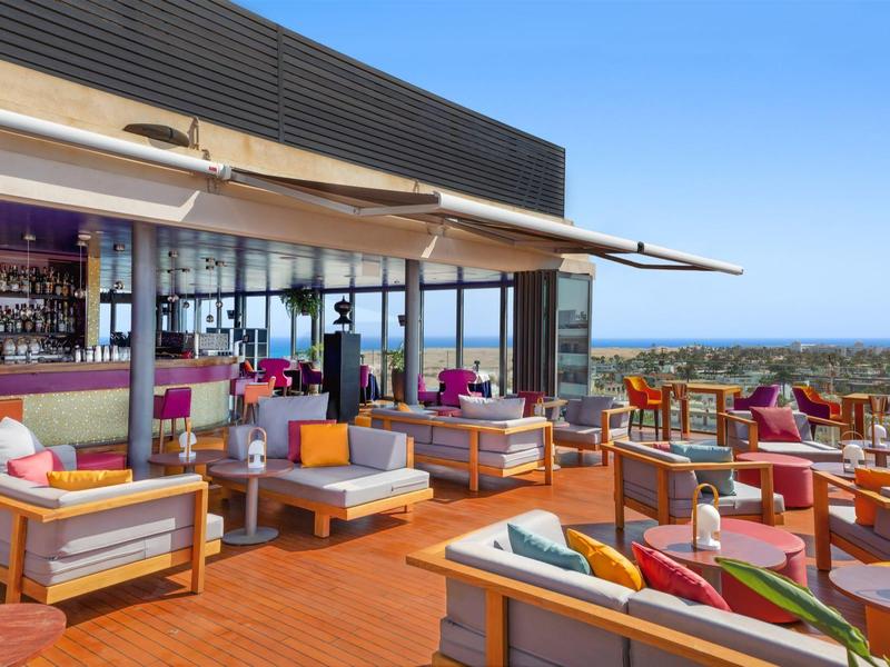 Area esterna del bar dell'hotel con posti a sedere moderni e vista sul mare sotto cielo sereno.