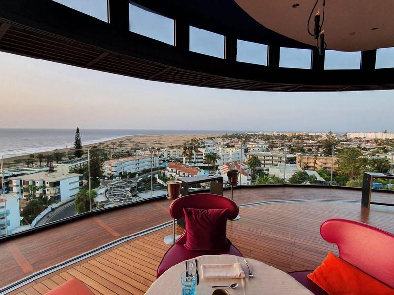 Terrazza panoramica con arredamento lounge rosso con vista sulla città costiera e sul mare al tramonto