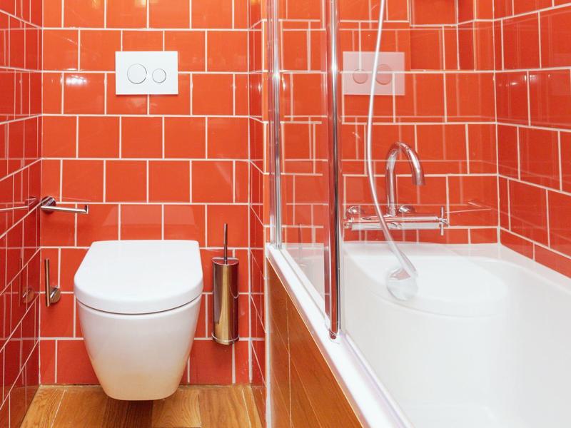 Bagno moderno con parete piastrellata rossa, WC bianco e vasca da bagno con pannello di vetro.