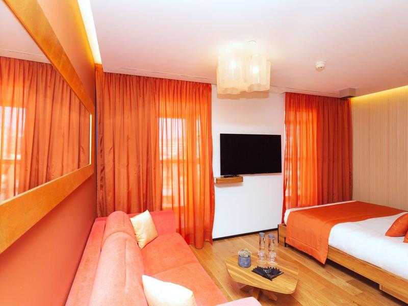 Camera d'hotel moderna con tende arancioni, divano e un grande letto.