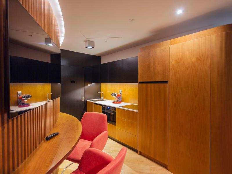 Camera d'hotel moderna con rivestimento in legno, poltrona rossa e illuminazione indiretta.