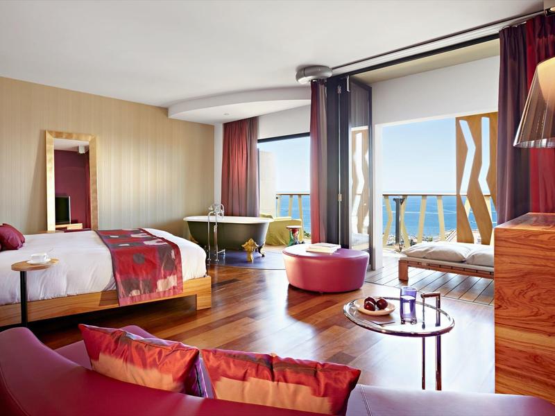 Camera d'hotel moderna con letto matrimoniale, zona soggiorno e vista mare.