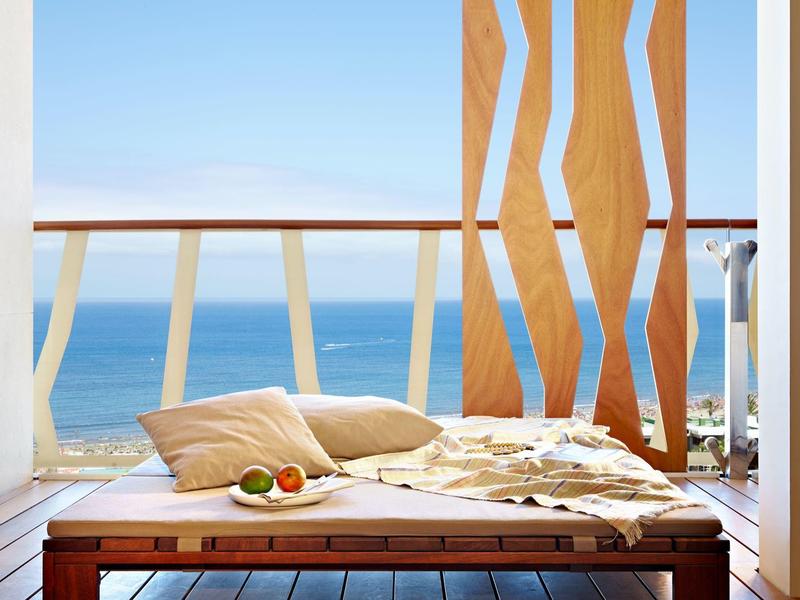Comoda sdraio con cuscini su balcone con vista sul mare e cielo limpido.