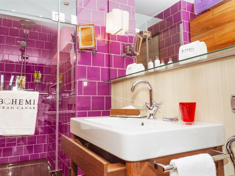 Bagno moderno con doccia piastrellata viola, lavabo e dettagli in legno.