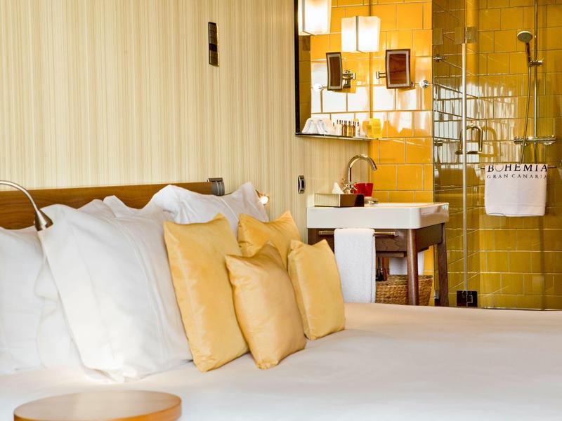 Camera d'hotel moderna con letto grande, più cuscini e bagno aperto.