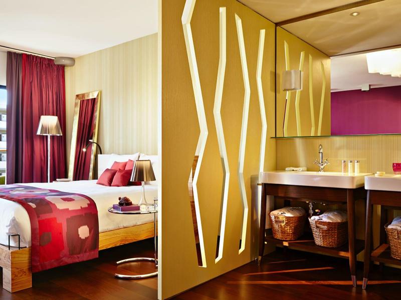 Camera d'hotel moderna con mobili in legno, letto matrimoniale e bagno elegante con grandi specchi.