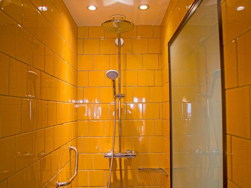 Doccia con piastrelle gialle, soffione doccia e parete in vetro in un bagno.