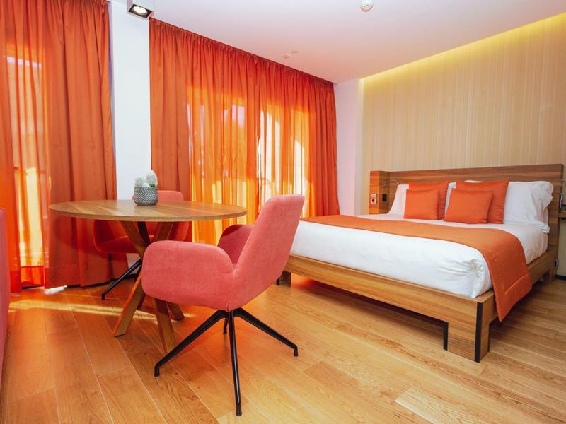 Camera d'albergo moderna con letto matrimoniale, pavimento in legno e accenti arancioni.