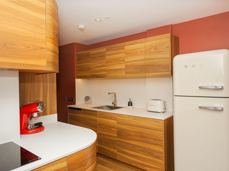 Cucina moderna con armadi in legno, macchina per caffè rossa e frigorifero retrò bianco.