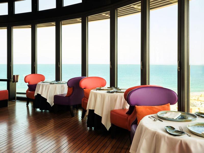 Elegante ristorante d'hotel con poltrone colorate e vista mare da grandi finestre.