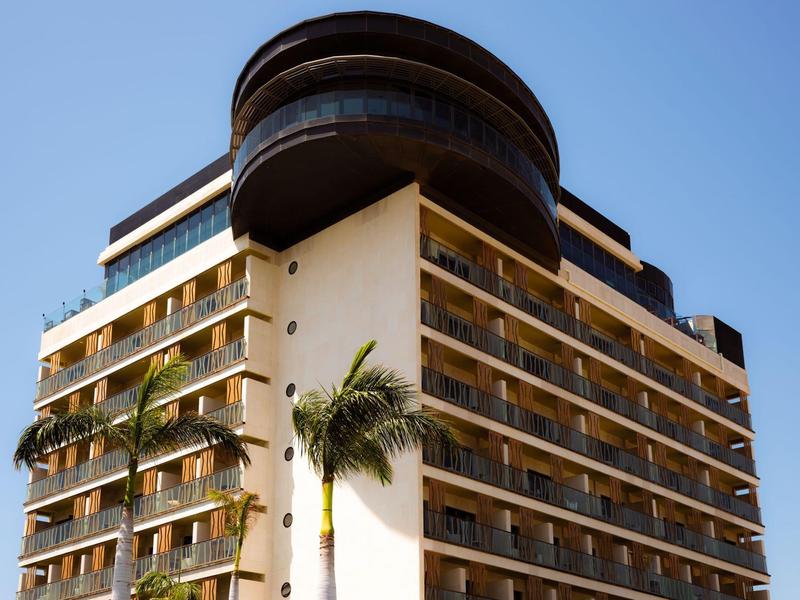 Hotel alto con balconi e palme sotto un cielo sereno.