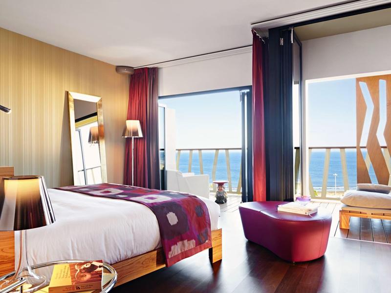 Camera d'hotel moderna con letto matrimoniale, balcone con vista mare e mobili di design.