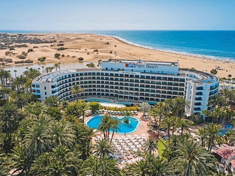 Gran hotel con piscina y palmeras en la playa con vista amplia al mar azul.