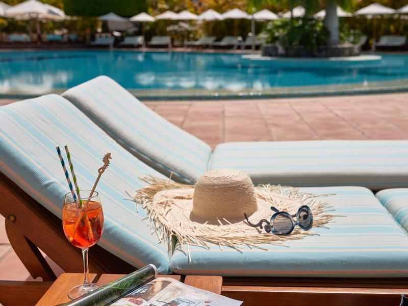 Dos tumbonas junto a la piscina con sombrero, gafas de sol y bebida en un día soleado.