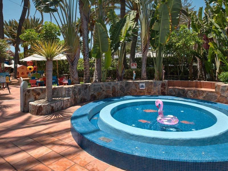 Una fuente circular azul con un flamenco en un jardín tropical de un hotel.
