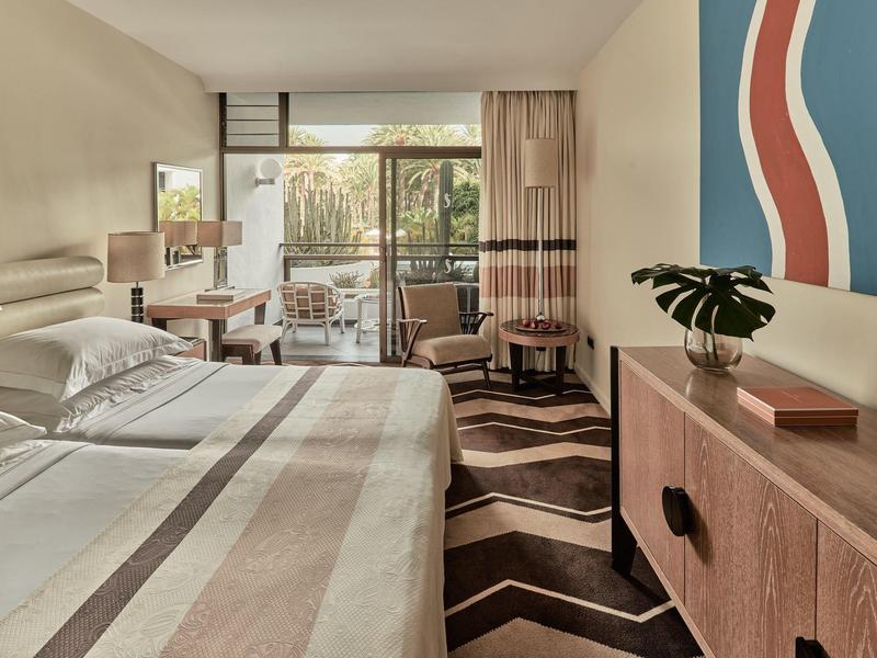 Habitación de hotel moderna con cama grande, escritorio, balcón y arte abstracto en la pared.