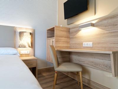 Moderner Hotelzimmerbereich mit Holzmöbeln, Stuhl, Bett und Wandfernseher.