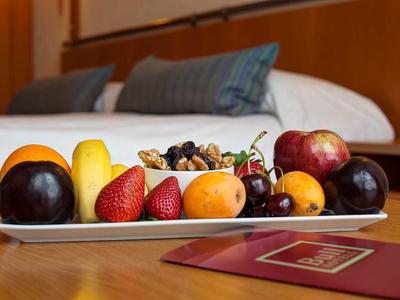 Talíř s různým čerstvým ovocem na stole v hotelovém pokoji vedle postele a pasu.