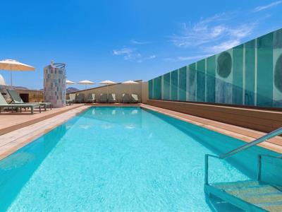 Moderner Hotelpool mit Liegestühlen, Umzäunung und blauem Himmel im Hintergrund.
