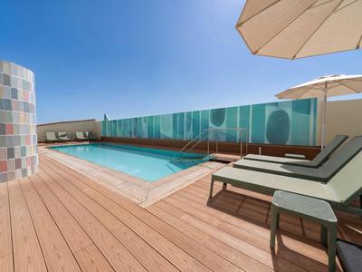 Moderner Dachpool mit Liegestühlen und Sonnenschirm auf Holzdeck bei klarem Himmel.