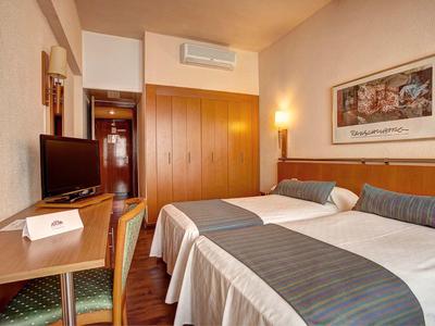 Pohodlný hotelový pokoj se dvěma postelemi, psacím stolem, skříní, televizí a teplým osvětlením.