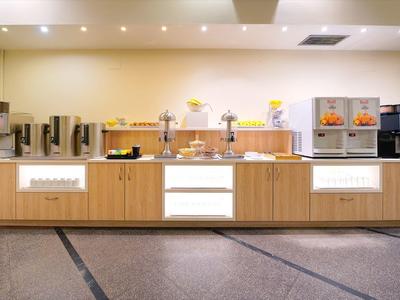 Moderní bufet se kávovary, dávkovači džusů a pečivem na dřevěném pultu.