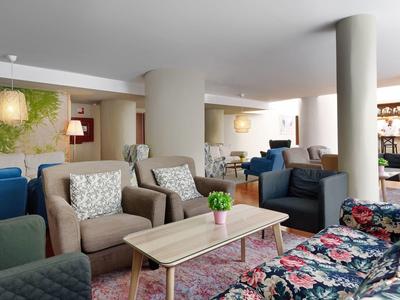 Jasná hotelová hala s květinovými pohovkami, křesly, dřevěnými stoly a dekorativními rostlinami.