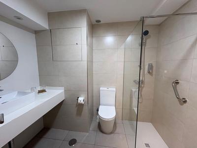 Helles Badezimmer mit weißem Waschbecken, Toilette und moderner Glastür zur Dusche.