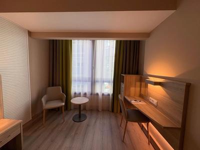 Modernes Hotelzimmer mit Holzfußboden, Schreibtisch, Stuhl und Fenster mit Vorhängen.