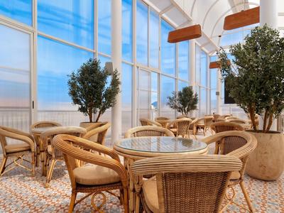 Heller Wintergarten mit Rattanmöbeln und großen Pflanzen, ideal für entspannte Hotelaufenthalte.