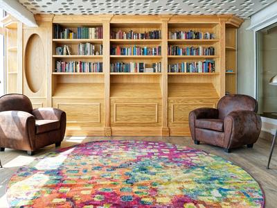 Gemütlicher Lesebereich mit zwei braunen Ledersesseln, bunter runder Teppich und Bücherregalen aus Holz.