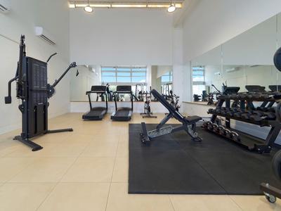 Heller Hotel-Fitnessraum mit Laufbändern, Gewichten und Kraftgeräten auf beigem Boden.