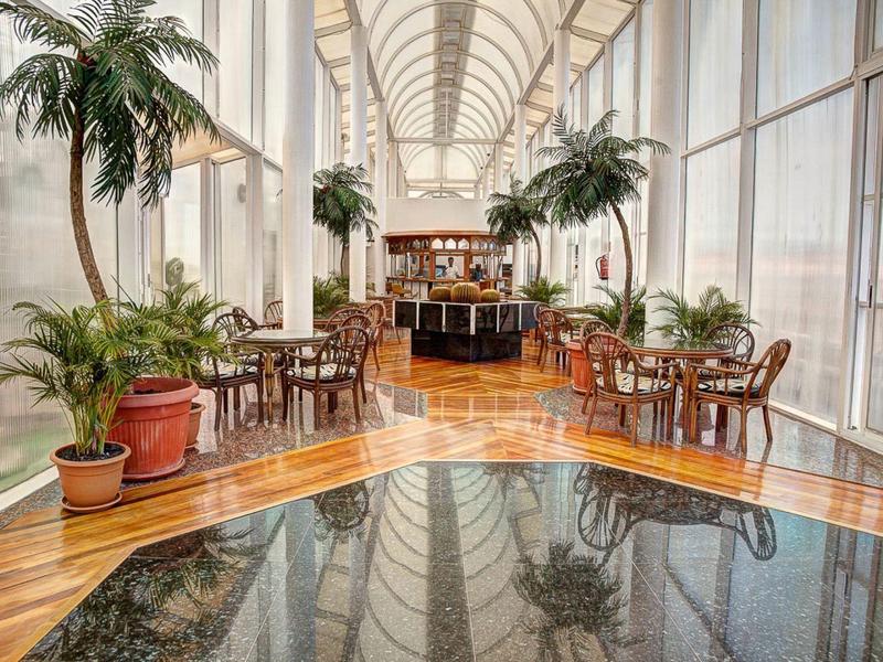 Luxusní hotelový salón s vysokými okny, vnitřními palmami a leštěnou dřevěnou podlahou.