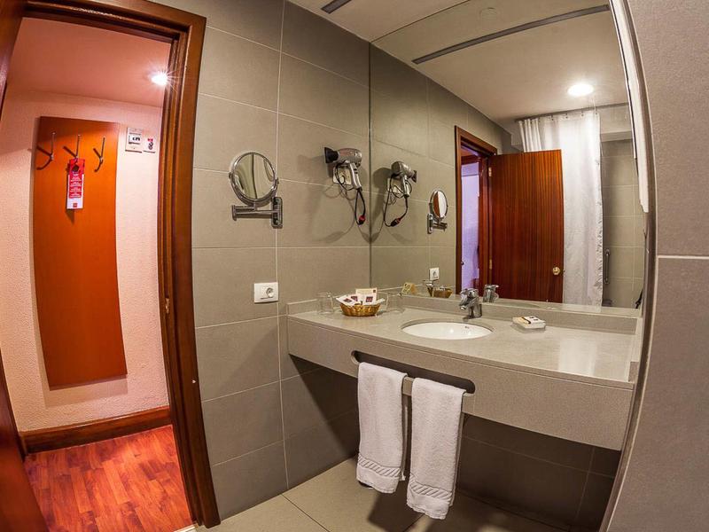 Moderní hotelová koupelna se dřezem, zrcadlem, ručníky a dřevěnými dveřmi.