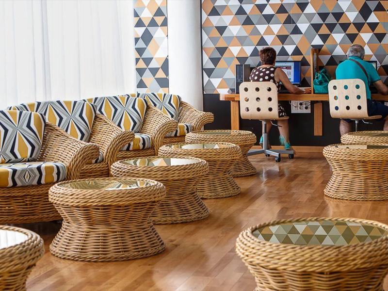 Světlý salonek s proutěnými stoličkami, vzorovanou pohovkou a geometrickým tapetem.