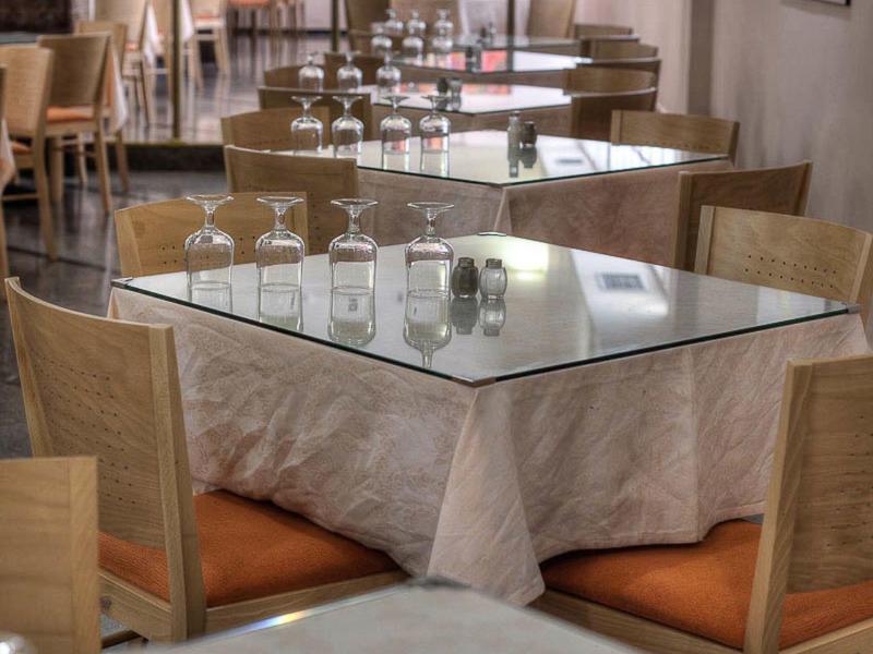 Světý interiér restaurace s prostřenými stoly a dřevěnými židlemi.